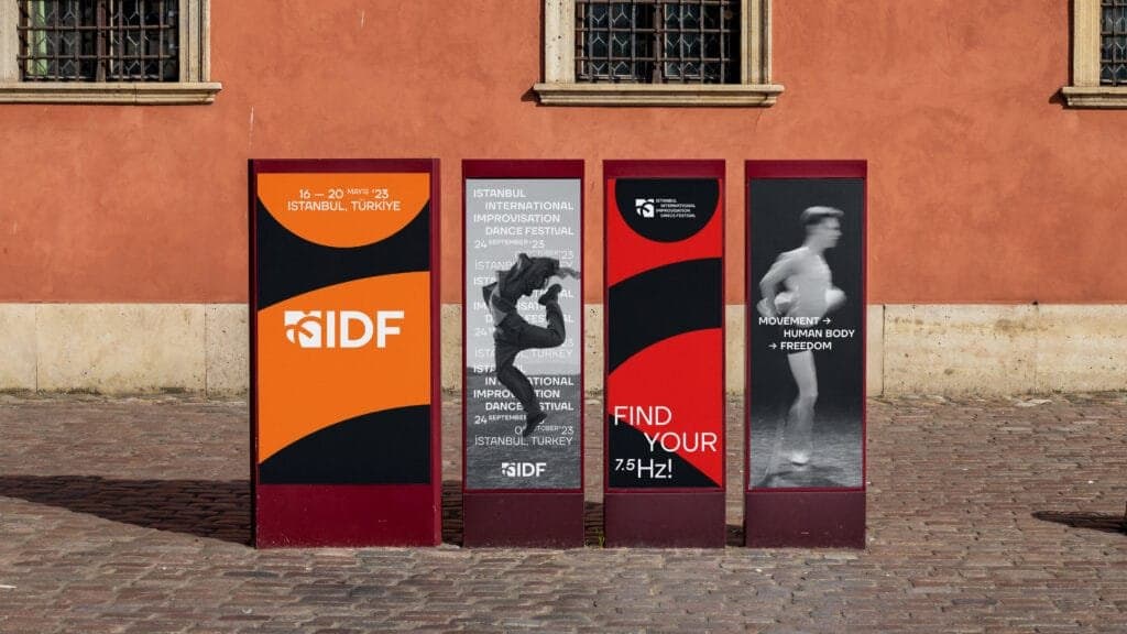 Street display of four vibrant posters promoting the Istanbul International Improvisation Dance Festival. The posters feature bold designs: one highlighting the festival dates, May 16–20, 2023; another showcasing a dynamic dancer mid-leap; a third with the tagline 'Find Your 7.5 Hz!'; and the fourth featuring a minimalist figure with the text 'Movement → Human Body → Freedom.' The colorful red and orange designs stand out against a rustic building backdrop.