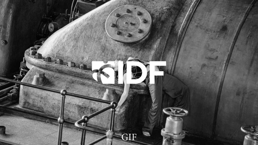 Black-and-white industrial setting featuring a dancer leaning gracefully on a large, weathered metal machine, overlaid with the bold logo 'IIDF,' representing the Istanbul International Improvisation Dance Festival.