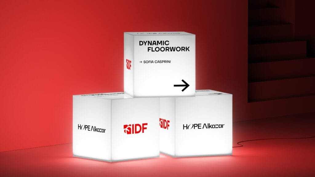 Modern installation of glowing white cubes against a bold red background, promoting the Istanbul International Improvisation Dance Festival (IIDF). The top cube displays 'Dynamic Floorwork by Sofia Casprini' with a directional arrow, while the lower cubes showcase the IIDF logo and the venue name 'Hope Alkazar,